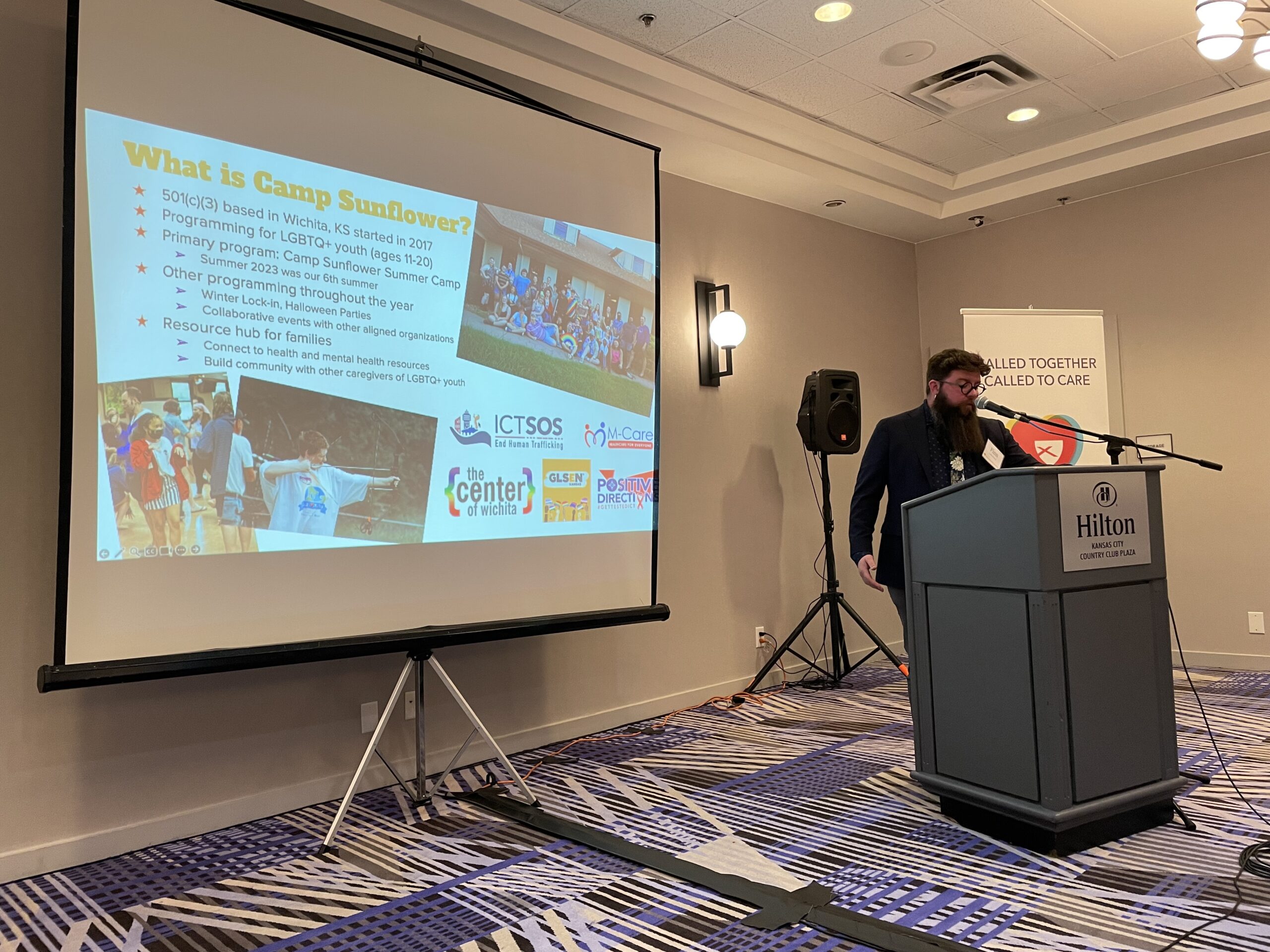Finn Lanning, Director of Camp Sunflower stands at a podium and presents a presentation of Camp Sunflowers impact. 